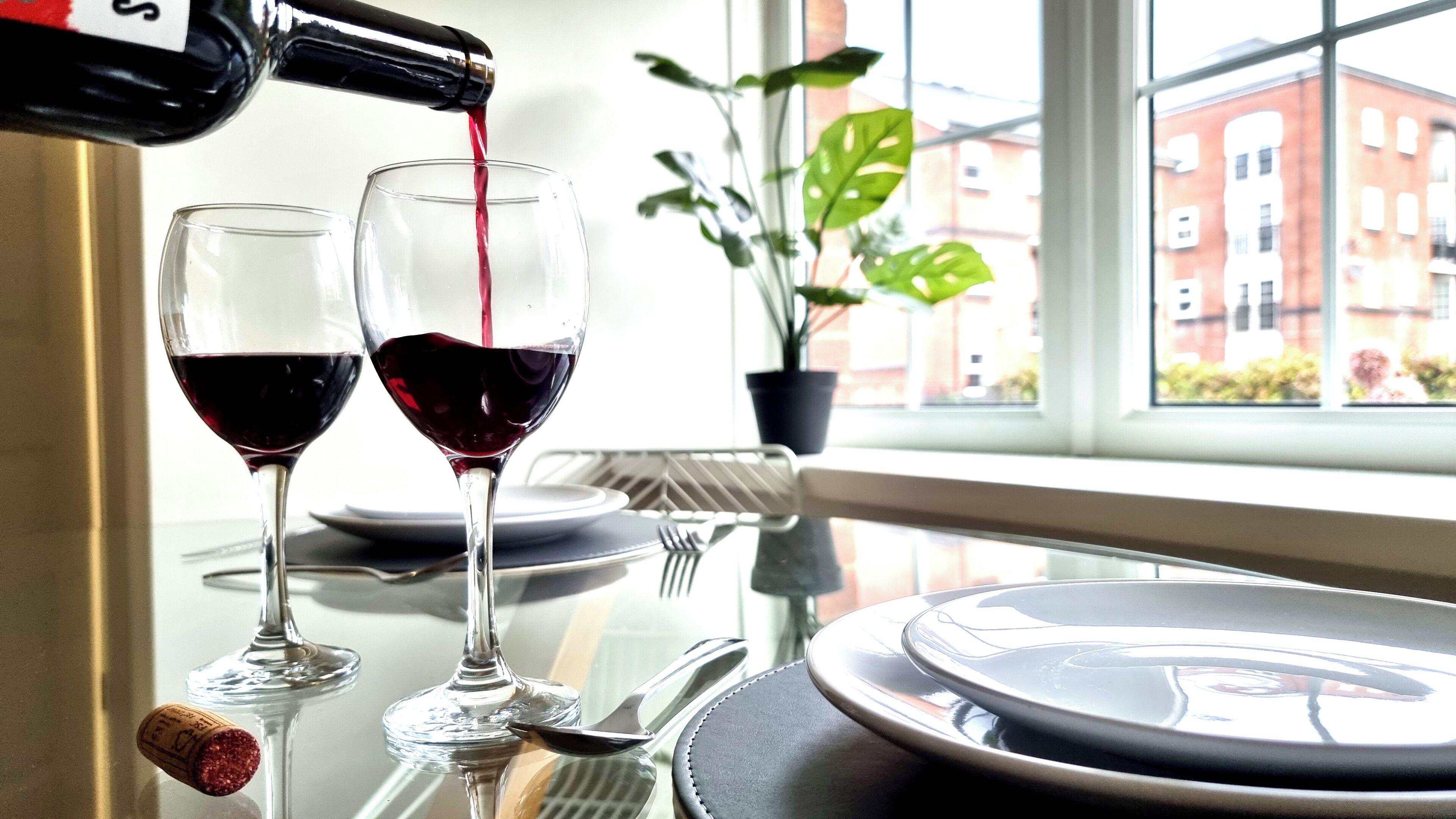 A table with two wine glasses, one being filled with red wine, and a bottle of red wine.