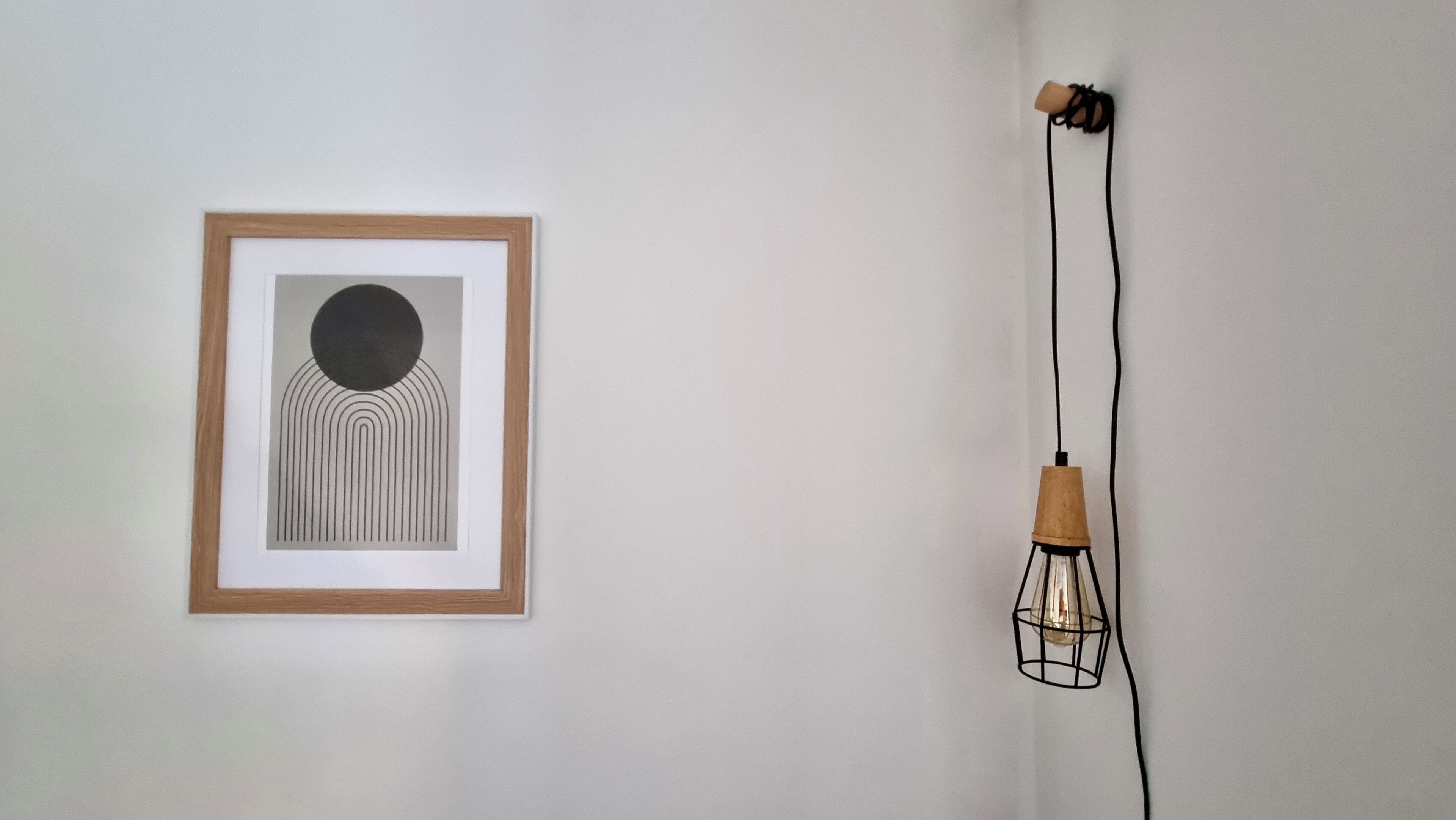Un'opera d'arte astratta incorniciata su una parete, un lampadario con base in legno e un cavo.