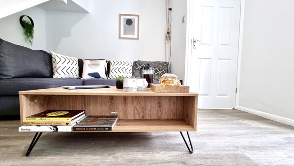 A wooden coffee table with books, a coffee maker, and a croissant on a wooden floor.