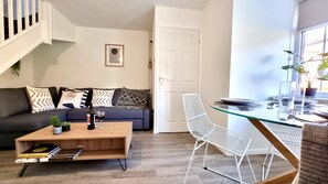 Un salon moderne comprenant un canapé, une table basse et un coin repas avec une table en verre et des chaises en métal.