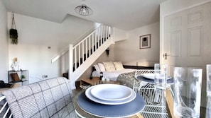 Un salon moderne avec un escalier, un coin repas avec de l’assiette et des verres, et un espace salon confortable avec un canapé à motifs.