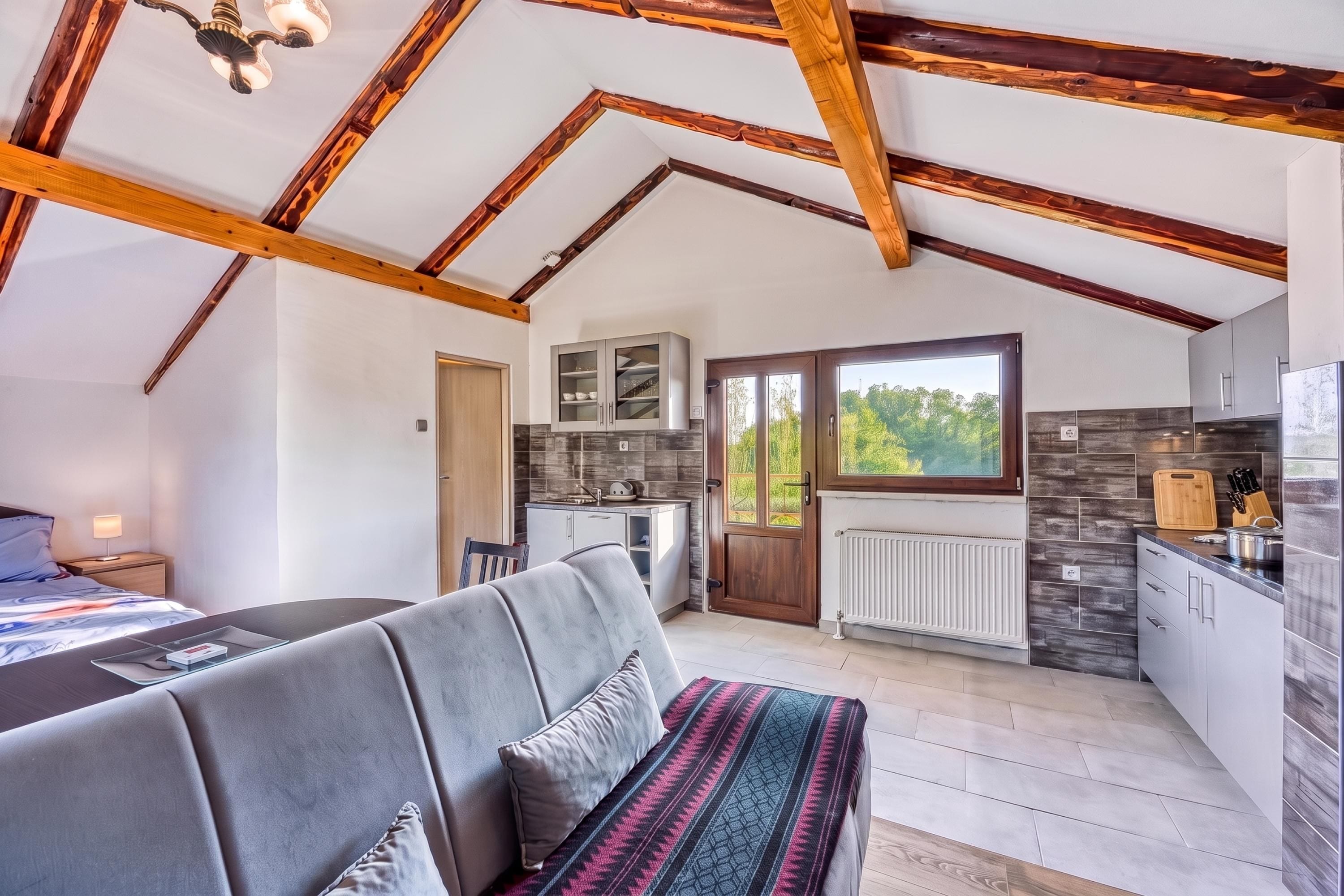 A modern interior with a high ceiling, exposed wooden beams, a sofa, a dining table, and a kitchen area.
