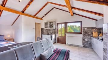 A modern interior with a high ceiling, exposed wooden beams, a sofa, a dining table, and a kitchen area.