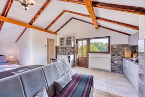 Un intérieur moderne avec un plafond haut, des poutres apparentes, un canapé, une table à manger et un coin cuisine.