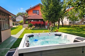 A hot tub in a backyard with a house, a gazebo, and a lawn.
