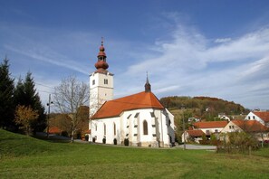 A church with a prominent bell tower and a red roof, surrounded by a green landscape and houses. - House Pepica With Hot Tub (Kraljevec na Sutli)