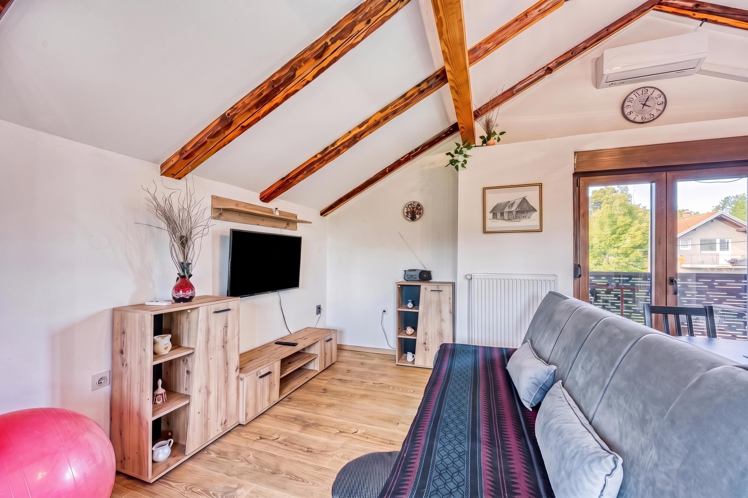 A modern living room with a wooden ceiling, a flat-screen TV, a sofa, and a small table with decorative items.