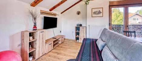 A modern living room with a wooden ceiling, a flat-screen TV, a sofa, and a small table with decorative items.