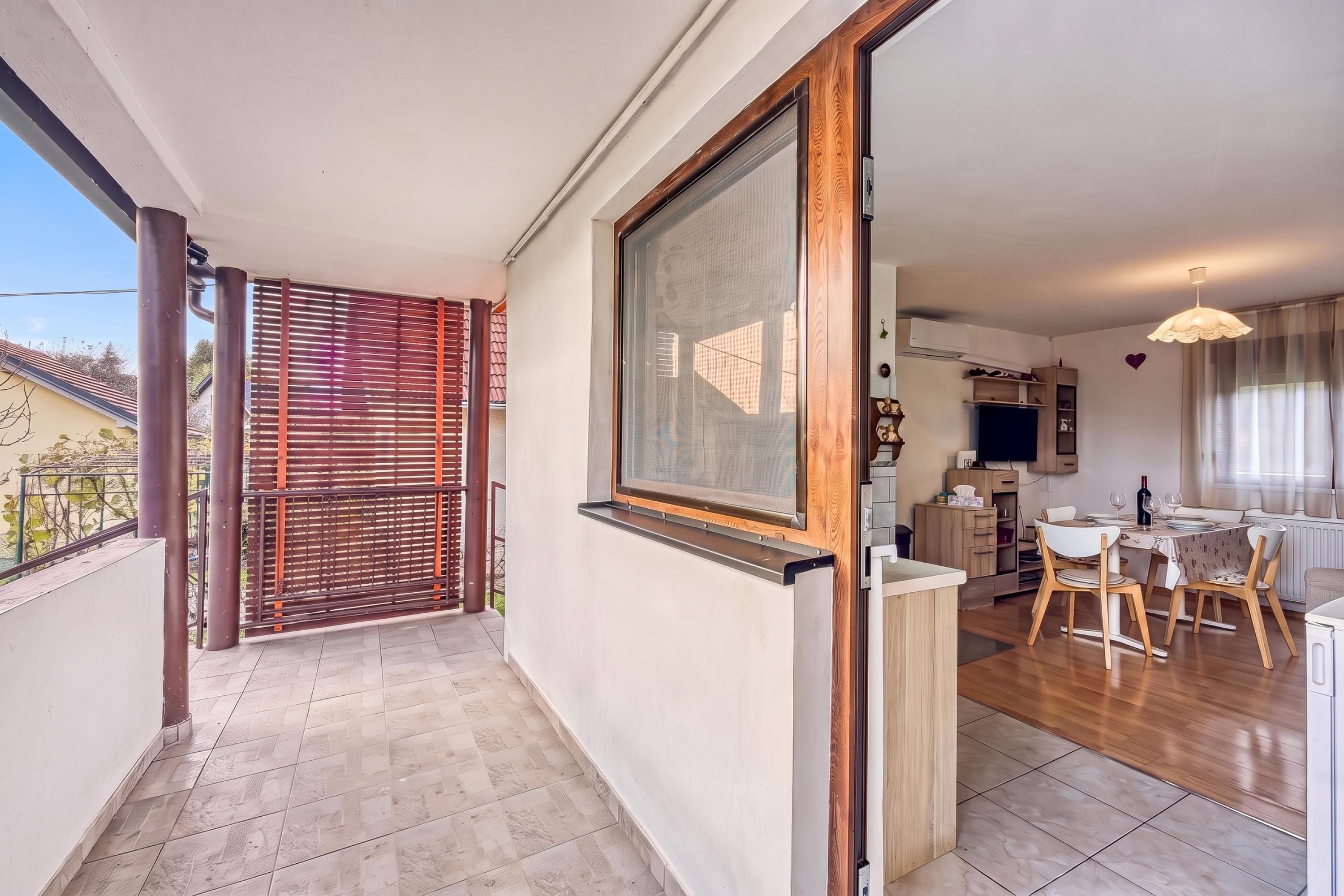 A balcony with a view of a neighboring building, a sliding glass door leading to a dining area, and a kitchen with a TV.