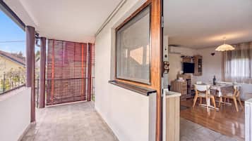 A balcony with a view of a neighboring building, a sliding glass door leading to a dining area, and a kitchen with a TV.