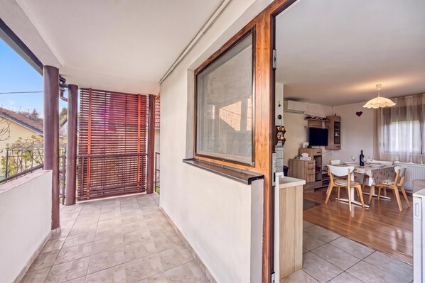 A balcony with a view of a neighboring building, a sliding glass door leading to a dining area, and a kitchen with a TV.