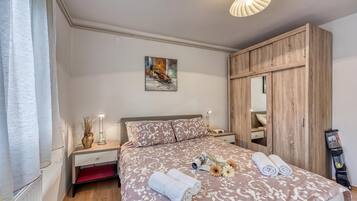 Une chambre à coucher comprenant un lit, des tables de chevet, une commode, un miroir, un luminaire au plafond et une fenêtre avec des rideaux.