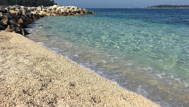 A pebble beach with clear water and a rocky outcrop in the distance. - Lovely apartment few minutes from the beach (Štinjan)