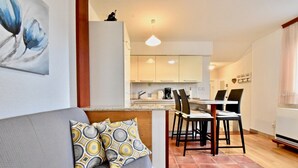 A modern living room with a grey sofa, patterned cushions, a dining area with a table and chairs, and a kitchen in the background. - Lovely apartment few minutes from the beach (Štinjan)