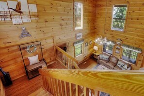 Interior de una cabaña de madera con un dormitorio en el altillo, una sala de estar con sofá y una mesa de comedor, y una escalera que sube al altillo.