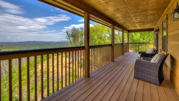 Un porche cubierto con una terraza de madera, una zona de estar con sillas acolchadas y vistas a un paisaje boscoso.