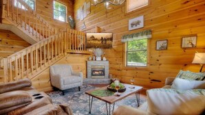 Un acogedor interior de cabaña de troncos con una escalera, una chimenea y una zona de estar confortable.