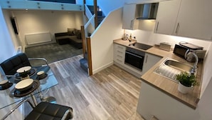 A modern kitchen with a built-in oven, a dining area with a glass table, and a staircase leading to a loft bedroom. - King Street Serviced Apartments (Lancaster)