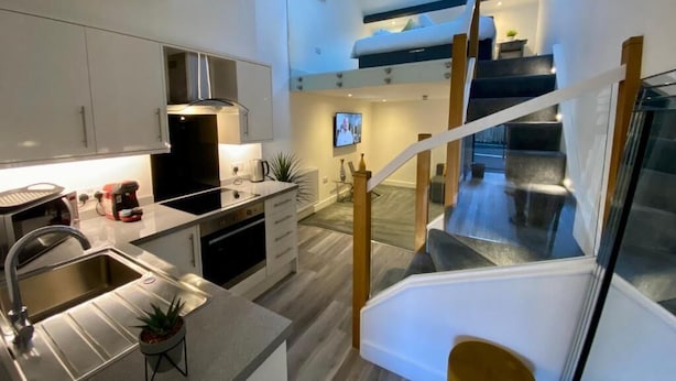 A modern kitchen with a built-in stove, a sink, and a dining area with a high table and chairs. - King Street Serviced Apartments (Lancaster)