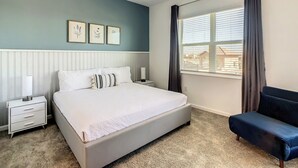 A bedroom with a bed, bedside tables, a nightstand, a window with curtains, and a view of buildings outside. - Family Fun: Waterpark & Game Room Condo! (Four Corners)