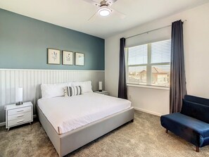 A bedroom with a bed, bedside tables, a nightstand, a window with curtains, and a view of buildings outside.