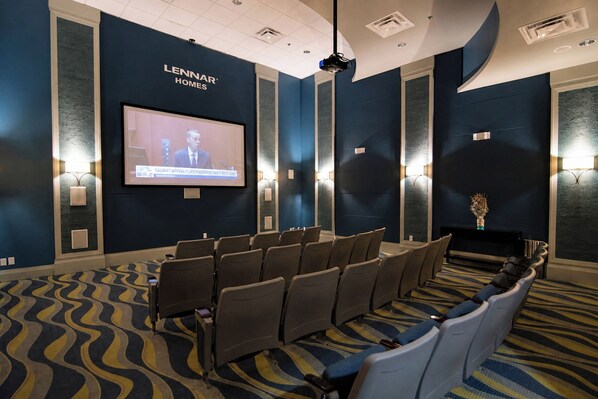 Une salle de conférence dotée d’un grand écran diffusant un journal télévisé, de rangées de chaises et d’un tapis à motifs.
