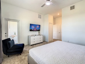 A bedroom with a bed, a dresser, a TV on the wall, and a door.