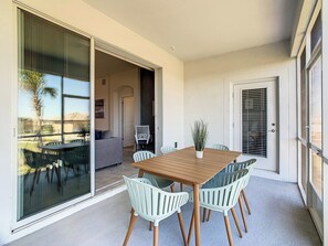 Un coin repas avec une table en bois et des chaises blanches, une plante en pot et une porte-fenêtre coulissante donnant sur un patio.