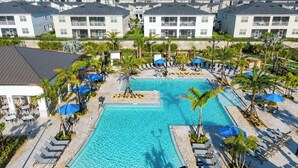 A resort with a central swimming pool surrounded by lounge chairs and palm trees, with multiple buildings in the background. - Family Fun: Waterpark & Game Room Condo! (Four Corners)