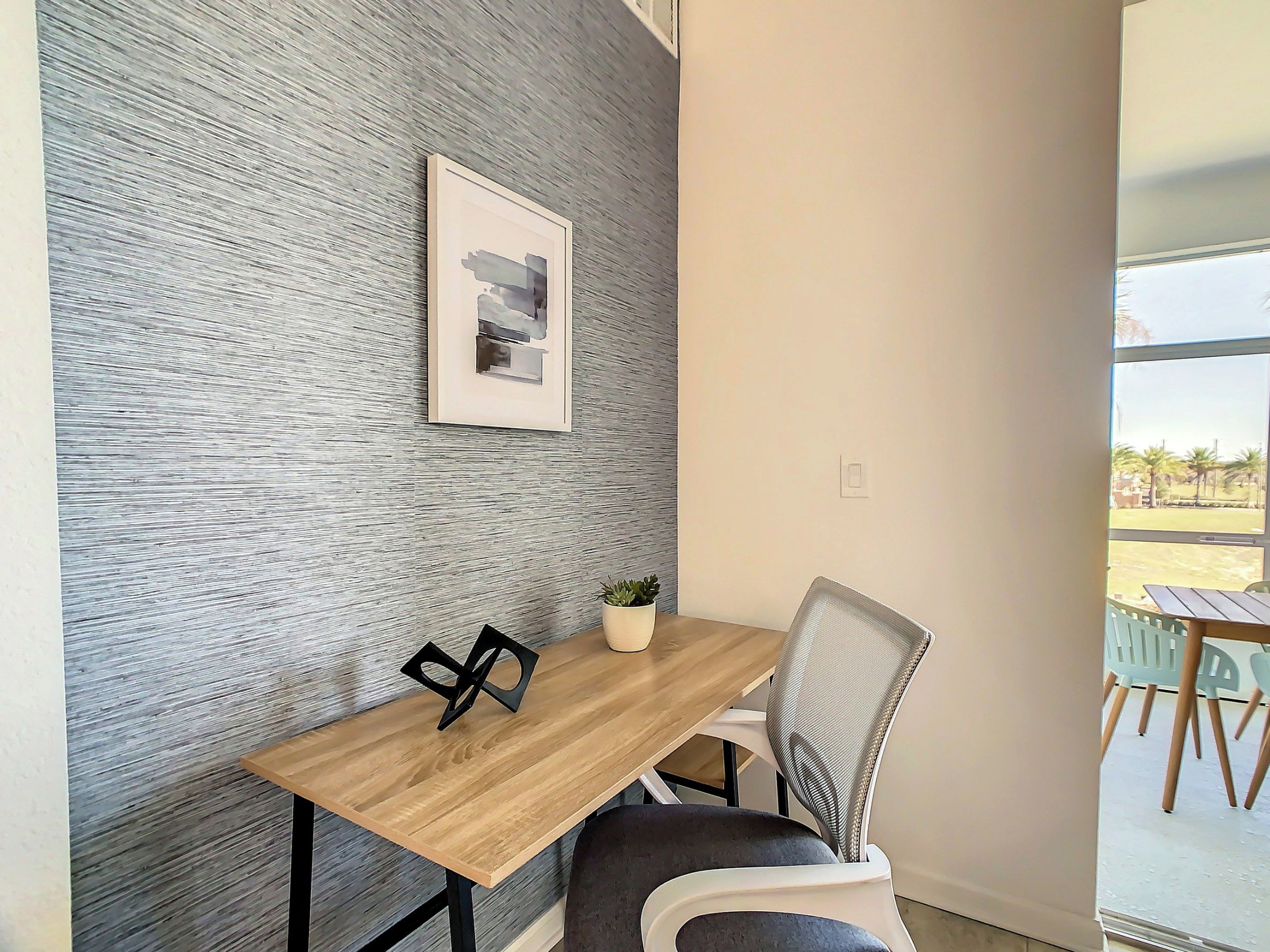 Een moderne kamer met een houten tafel, een potplant, een ingelijste foto en uitzicht op het groen.