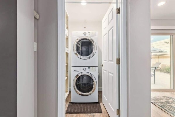 A laundry room with two stacked front-loading washing machines, a door leading to an outdoor area, and a small rug on the floor.