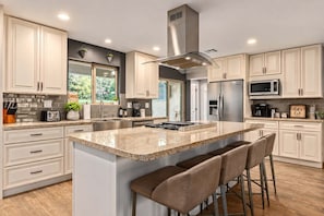 A modern kitchen with a large island, stainless steel appliances, and a view of the outdoors.