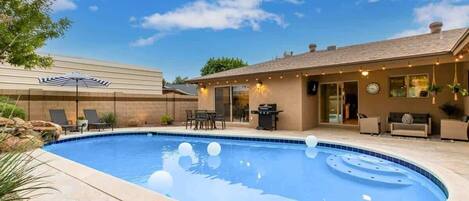 Una piscina con borde curvo, mobiliario de exterior y un patio con una parrilla.