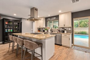Una cocina moderna con una isla central, taburetes de bar, electrodomésticos de acero inoxidable y vistas a una piscina.