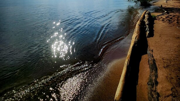 Een strand met een houten paal en rustig water dat zonlicht weerkaatst.