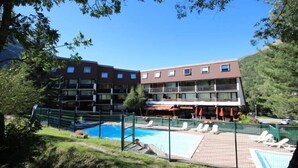 Un hotel con varios pisos, piscina al aire libre y sillas de descanso.