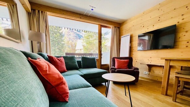 Una sala de estar acogedora con un sofá modular, una mesita redonda y un televisor instalado en la pared.