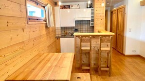 Cocina compacta con paredes de madera, una ventana y un pequeño comedor con un banco y dos sillas.