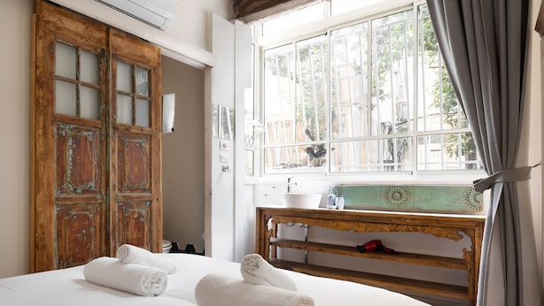 Ein Hotelzimmer mit Bett, Holzschrank, einem Fenster mit Vorhängen und einem Nachttisch mit Waschbecken.