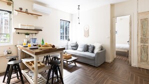 Eine moderne Küche mit einer Holzinsel, Barhocker und einem grauen Sofa in einem hellen Wohnbereich mit Holzboden und einem großen Fenster.