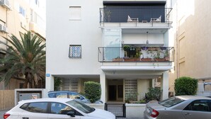 Ein zweistöckiges Wohngebäude mit einem Balkon im oberen Geschoss, einem verschlossenen Eingangsbereich und einer Palme im Vordergrund.