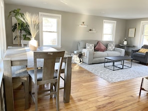 Una sala de estar con un sofá gris, una mesa de centro y un comedor con una mesa y sillas de madera.