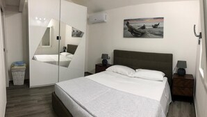Ett sovrum med en säng, två sängbord, en spegel och en tavla med motiv av båtar på väggen.