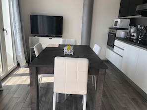 A modern kitchen with a dining table, chairs, a flat-screen TV, and a microwave.