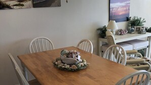 Un comedor con mesa de madera, sillas blancas, una lámpara de araña y decoración en la pared.