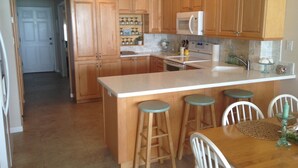 Una cocina con armarios de madera, microondas, fregadero y zona de comedor con taburetes y sillas.