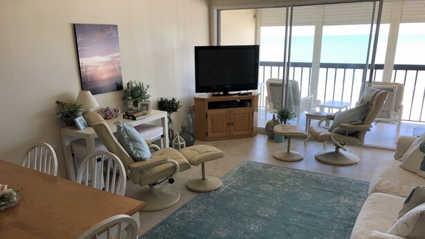 Una sala de estar con televisor, asientos cómodos, zona de comedor y vista al océano.