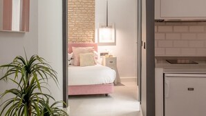 A bedroom with a brick wall, a bed with pink bedding, a bedside table with a lamp, and a small cabinet.