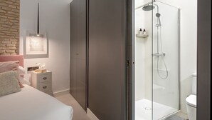 A modern bedroom with a bed, bedside table, and a glass-enclosed shower area.