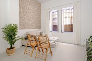 Een lichte woonkamer met een witte baksteenmuur, een bank, twee rieten fauteuils, een bijzettafeltje en een potplant.